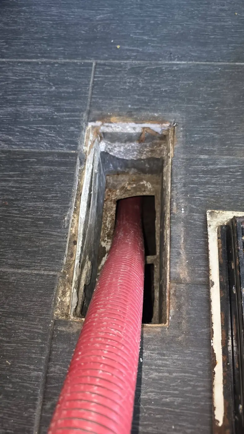 Negative-air vacuum hose running into a floor duct during cleaning